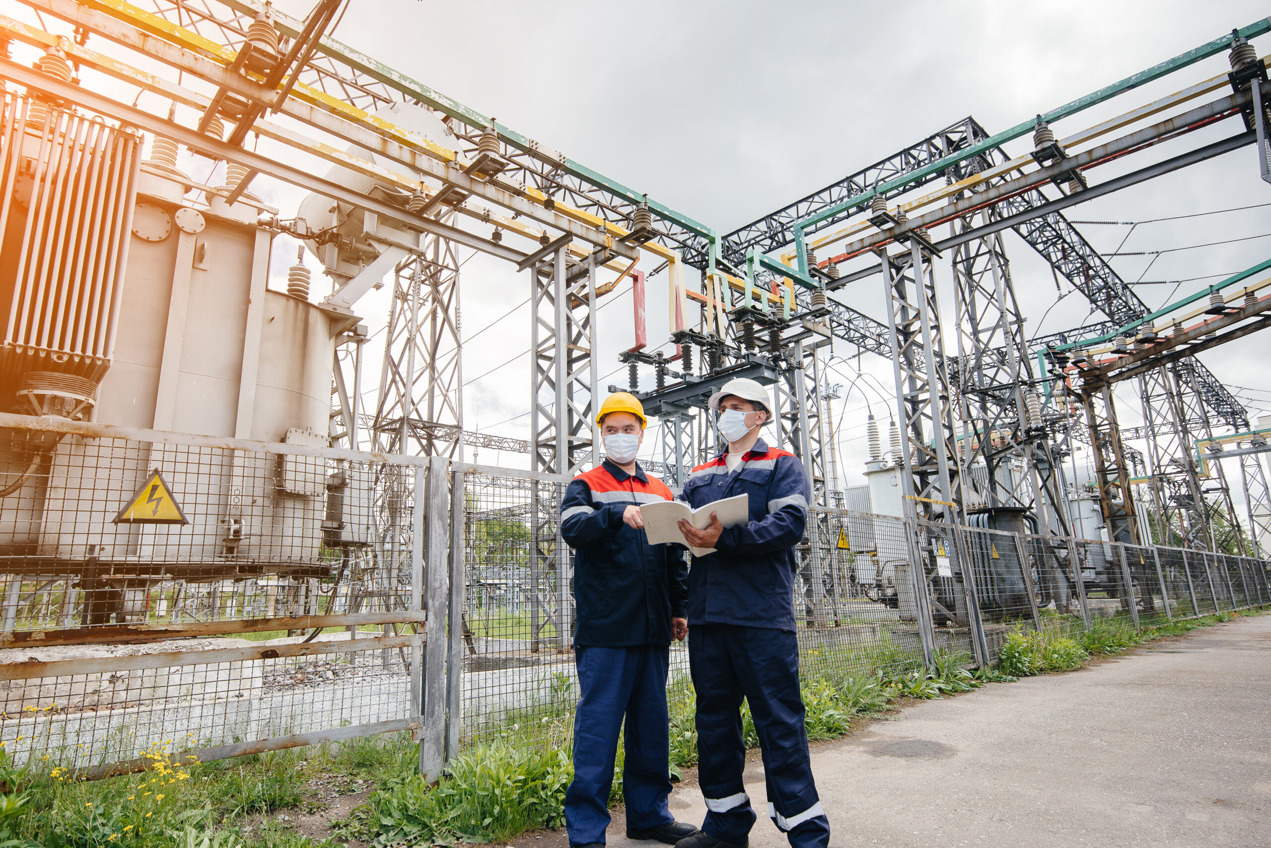 Engineers electrical substations conduct a survey of modern high-voltage equipment in the mask at the time of pandemia in the evening. Energy. Industry.